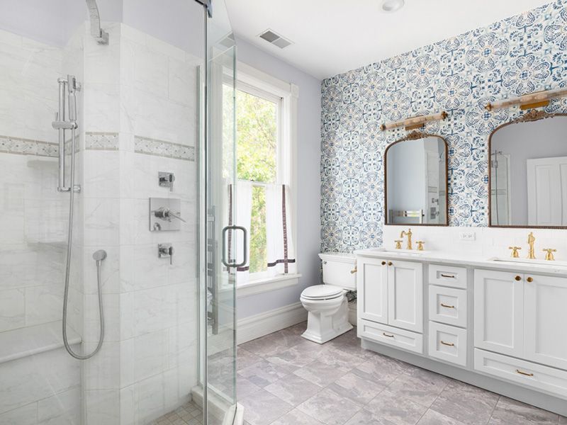 Bright modern bathroom with tiled shower, double vanity, large mirrors, and floral wallpaper accent wall