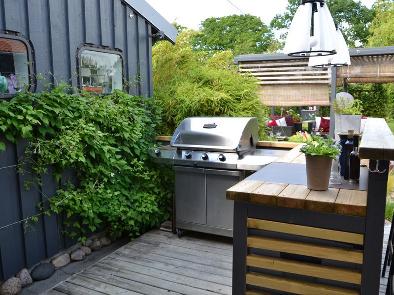 Outdoor patio with a stainless steel grill, wooden table, and potted plants beside a vine-covered wall