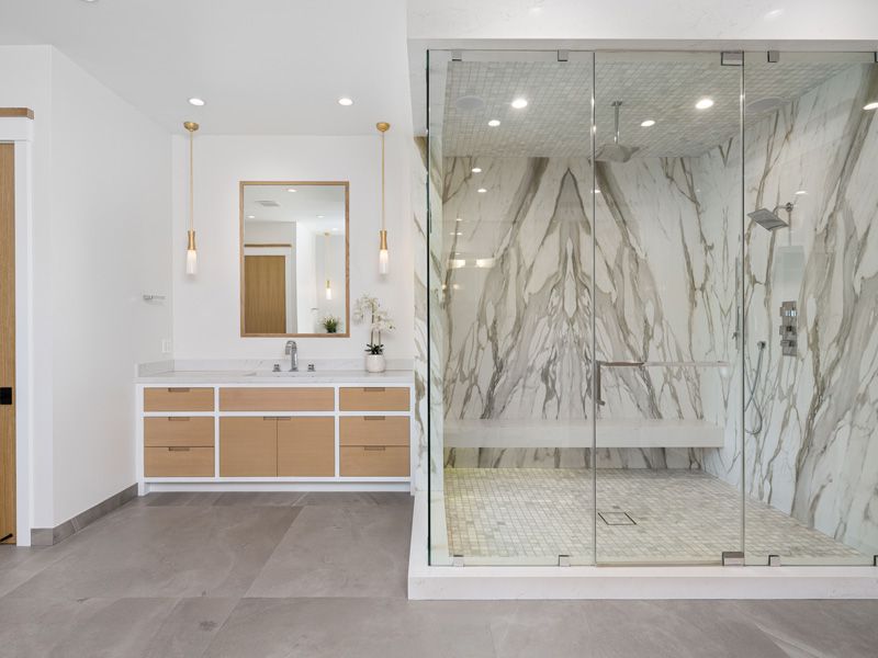 Modern bathroom with marble shower, glass doors, and white vanity with wood drawers