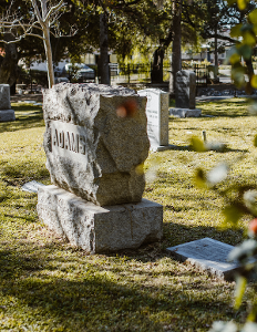 Weathered stone grave marker in a sunny cemetery with grass and trees