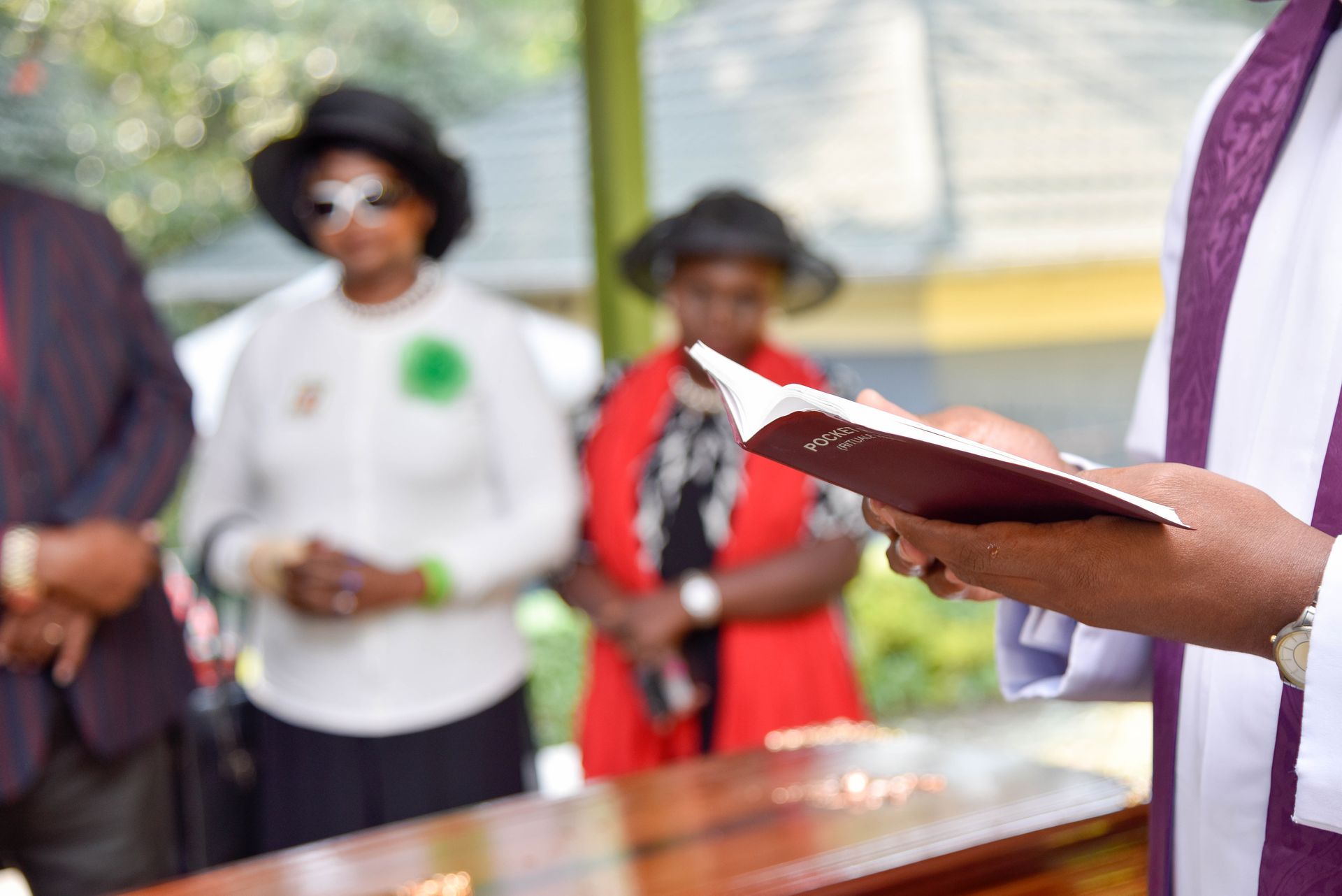 Person holding an open book during an outdoor gathering, with others standing blurred in the background.