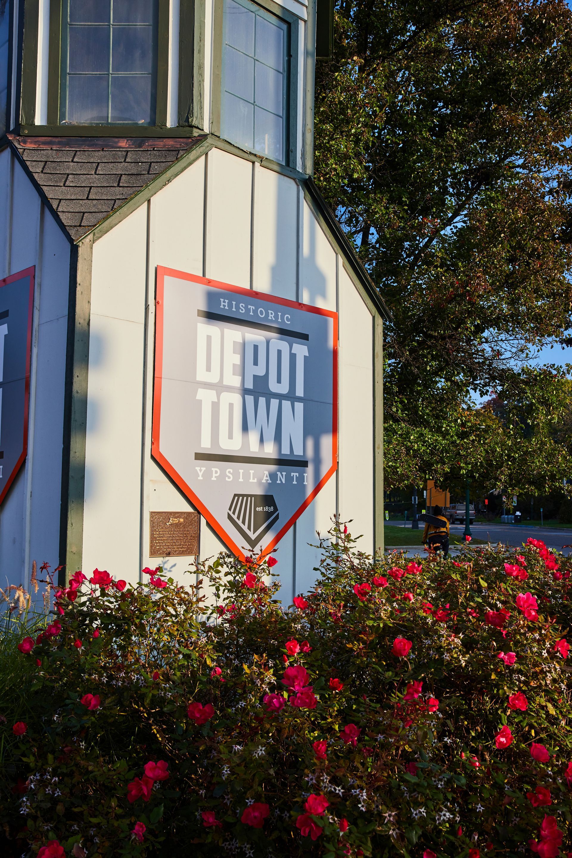 Depot Town sign on a white building, bordered by red flowers and trees in sunlight