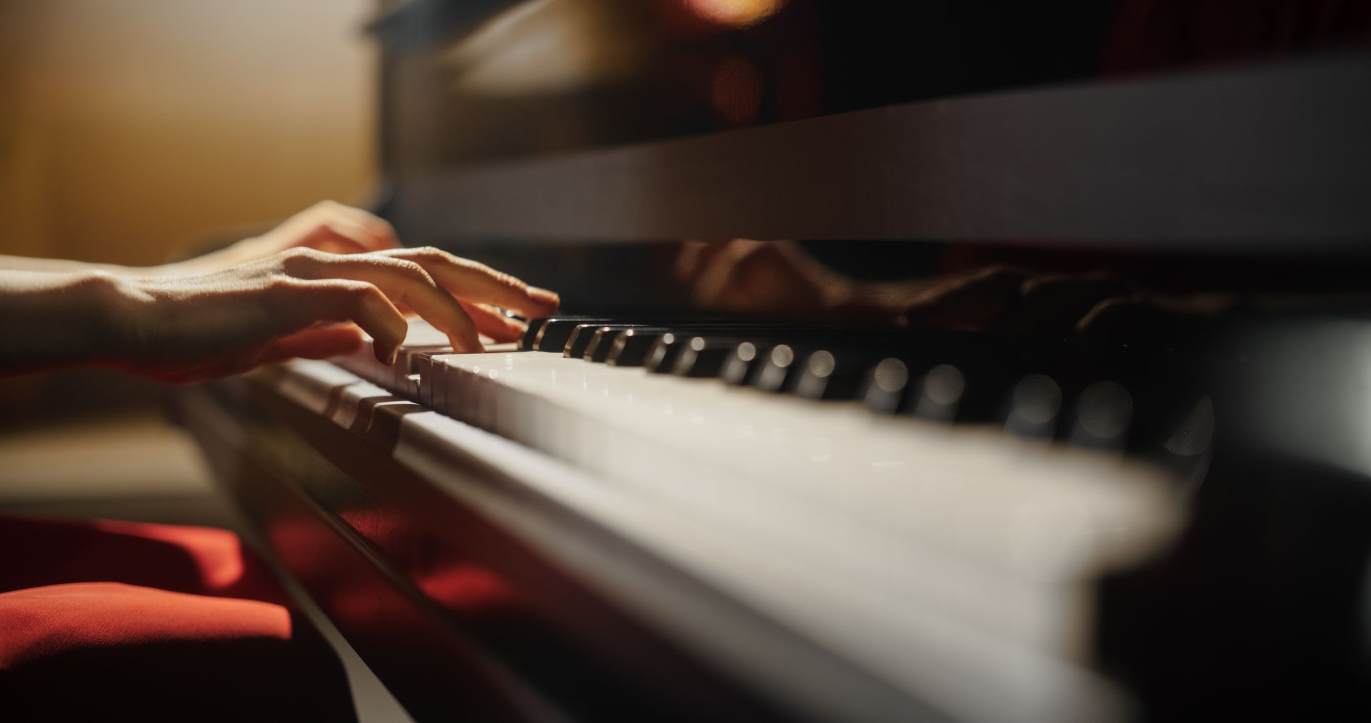 Hands playing a piano keyboard in warm, low light