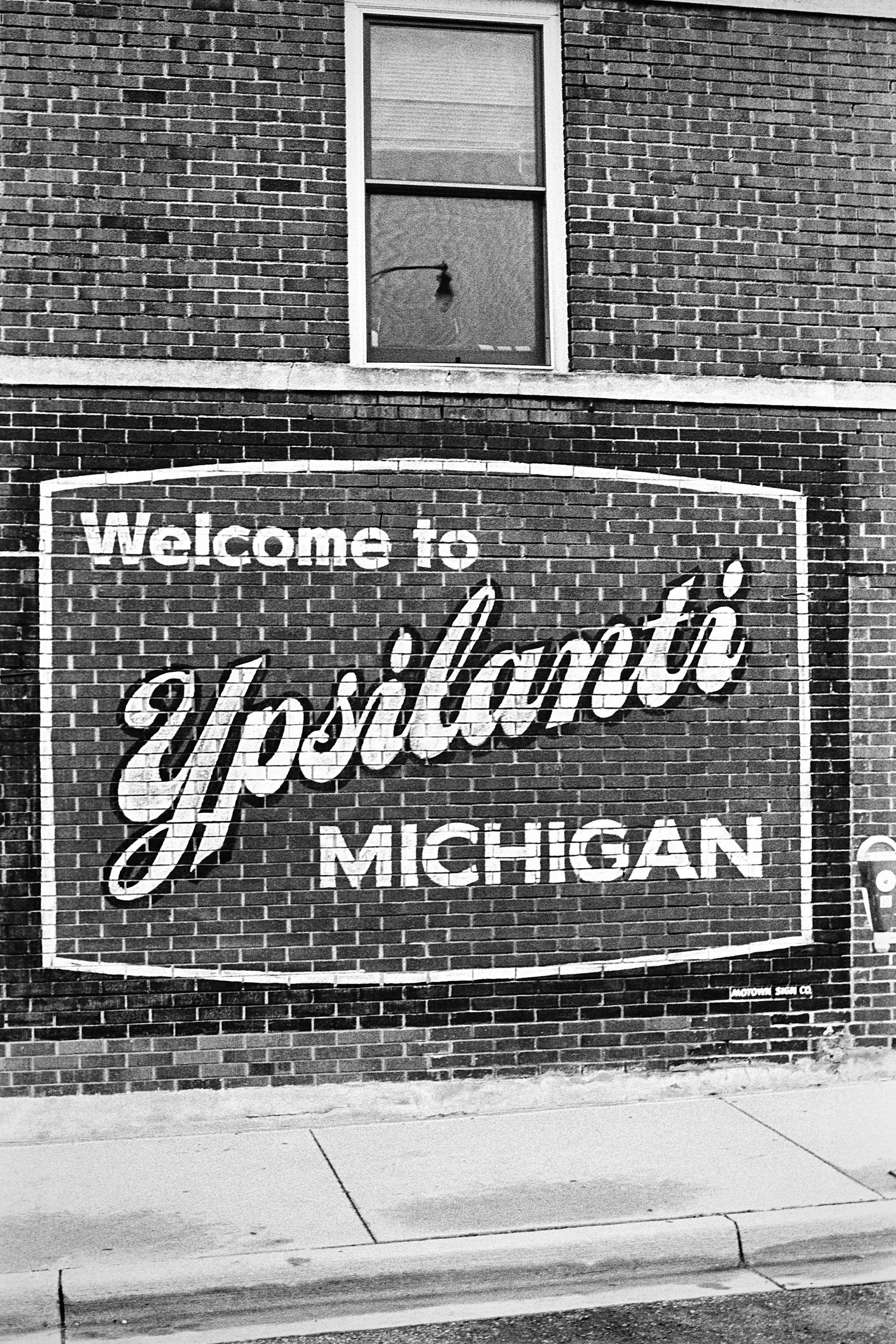 Black-and-white mural reading “Welcome to Ypsilanti, Michigan” on a brick wall.