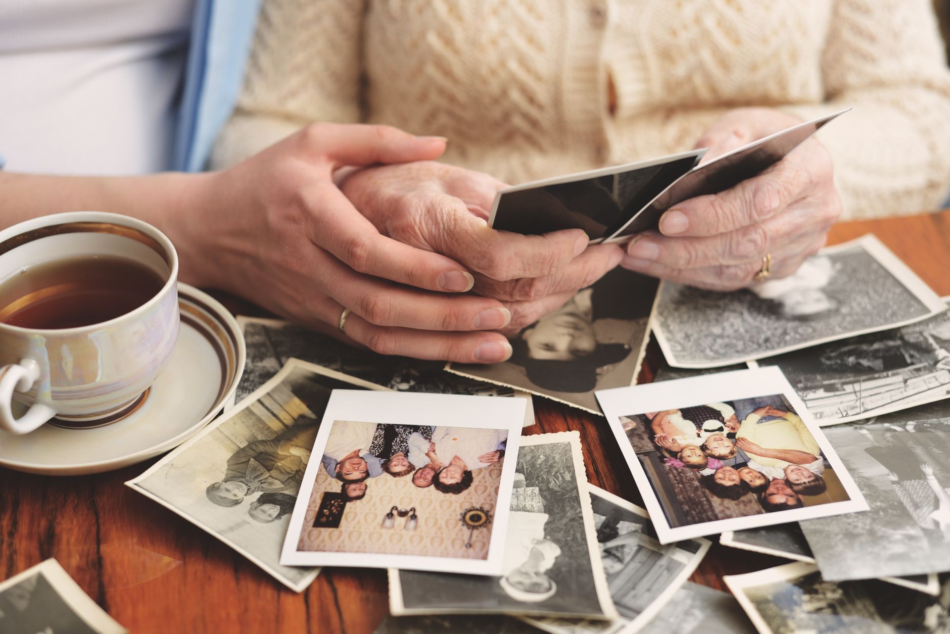 Hands sorting through printed photos beside a coffee cup on a table