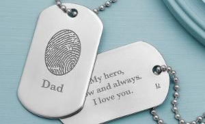 Dog tags on a blue surface, one engraved “Dad” with a fingerprint and one saying “My hero, my always, my love you.”