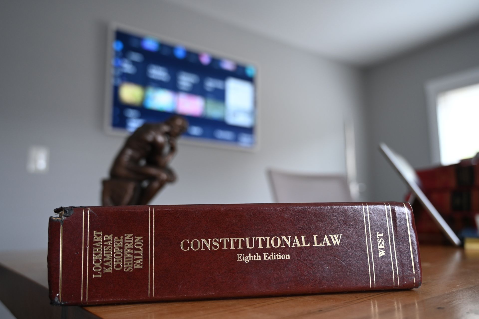 A red law book on a desk with a blurred courtroom statue and TV screen in the background