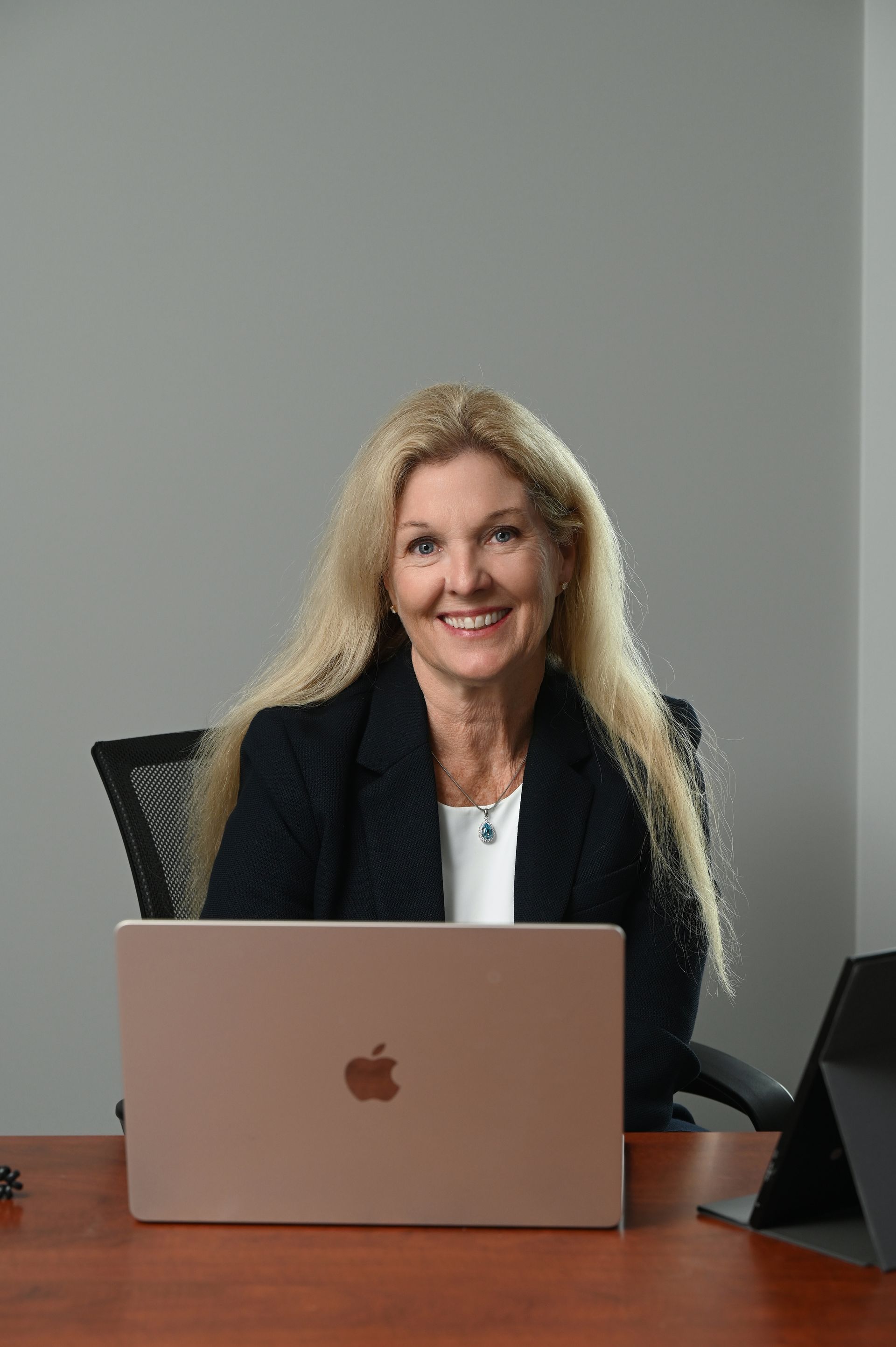 Woman smiling behind a rose-gold laptop in a conference room