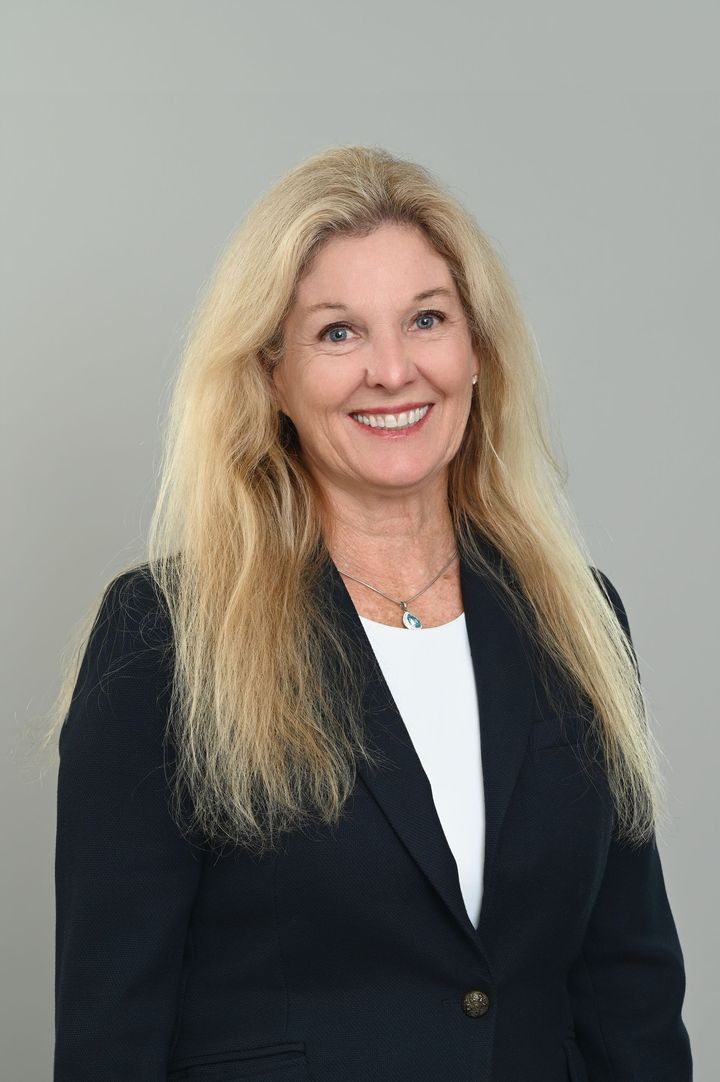 Smiling woman in a black blazer and white blouse against a gray background