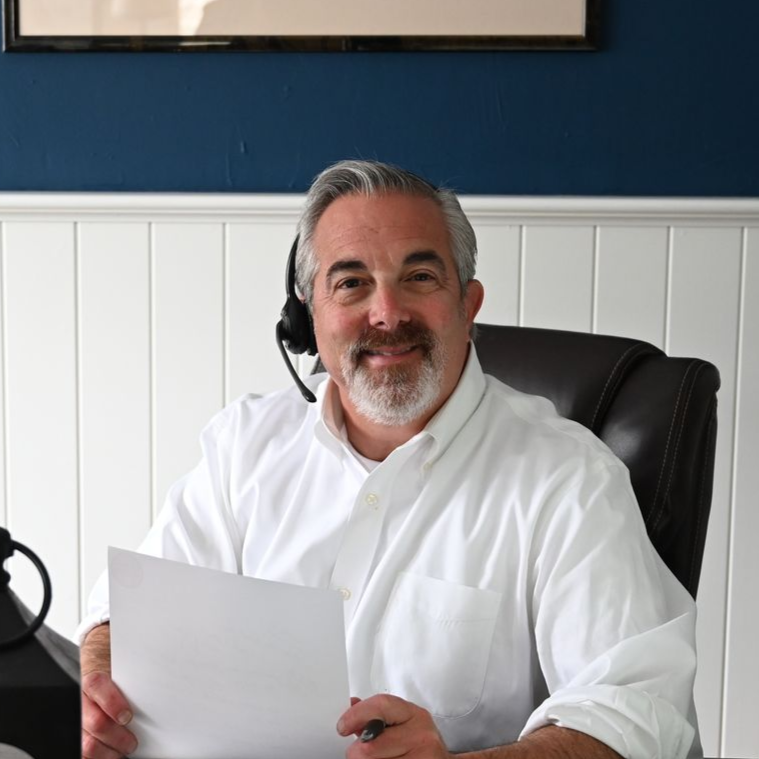 Robert Adelman smiling and holding a phone to his ear in a home office, wearing a dark sweater.