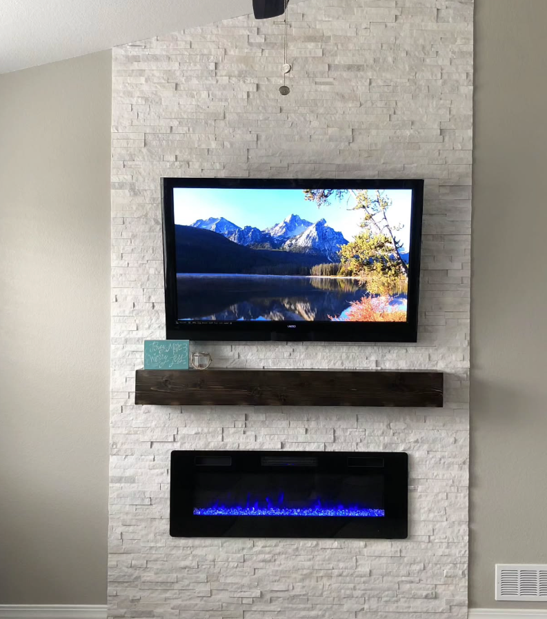 Wall-mounted TV above a shelf and electric fireplace on a white brick accent wall