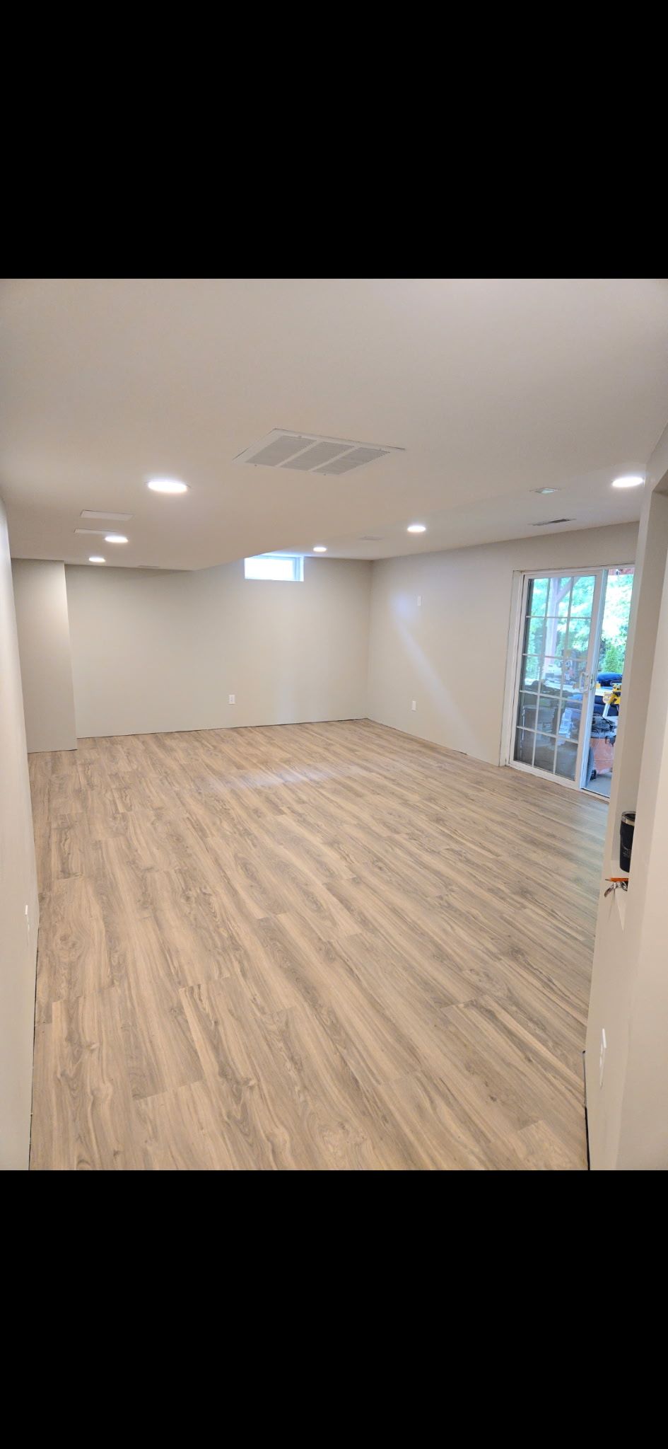Empty beige room with wood-look flooring, recessed ceiling lights, and a glass door to the outside.