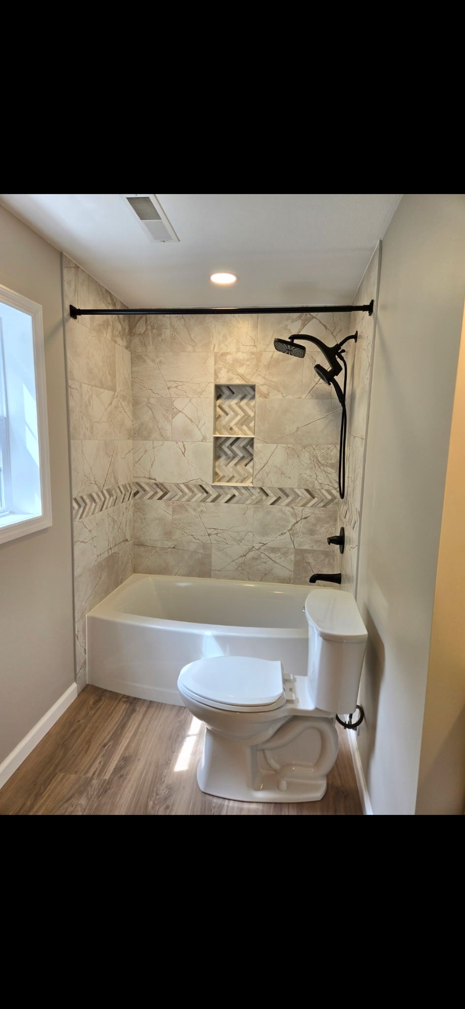 Bathroom with white shower-tub, beige tile wall, and window on the left.