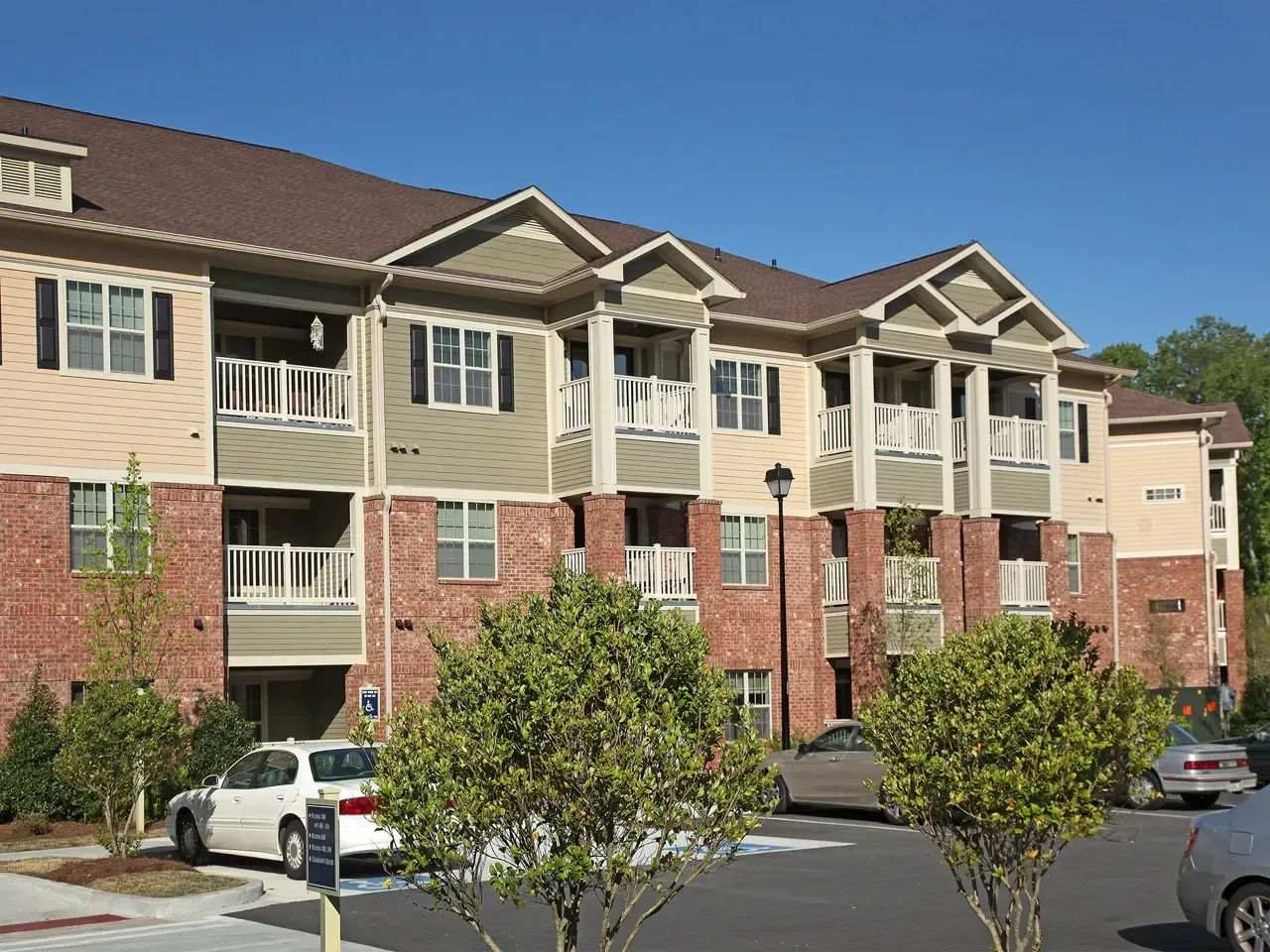 Exterior view of a multi-story apartment complex with brick lower level, beige siding, and balconies