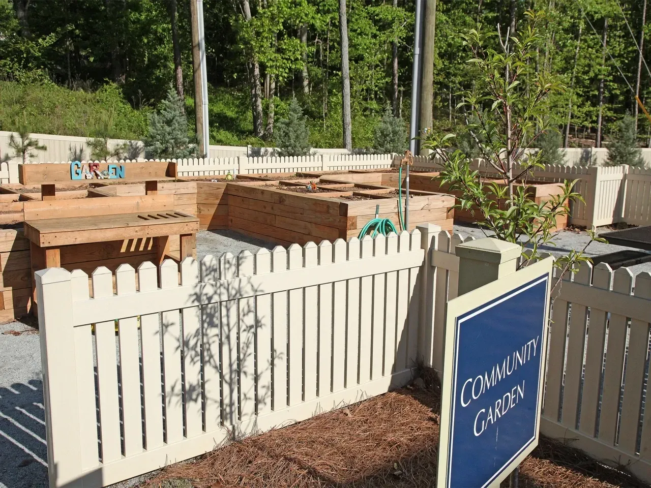 Raised wooden garden beds behind a white picket fence in a community garden.