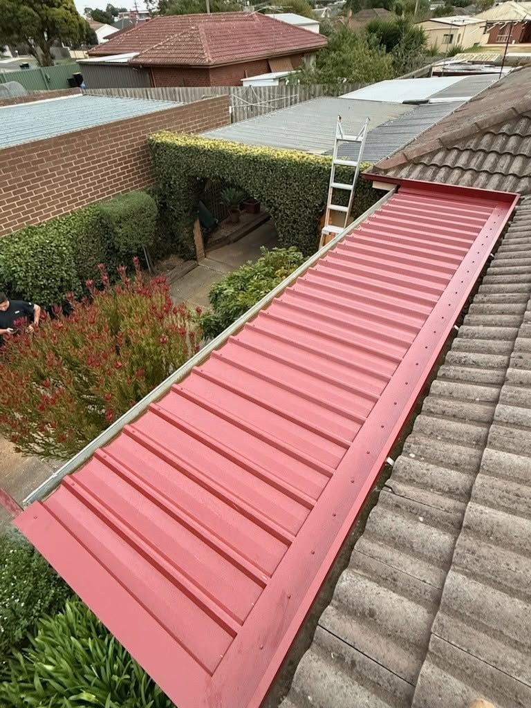 Red Metal Awning or Walkway Roof Between Tiled Rooftops in a Residential Yard — Kerney Plumbing in Caroline Spring, VIC
