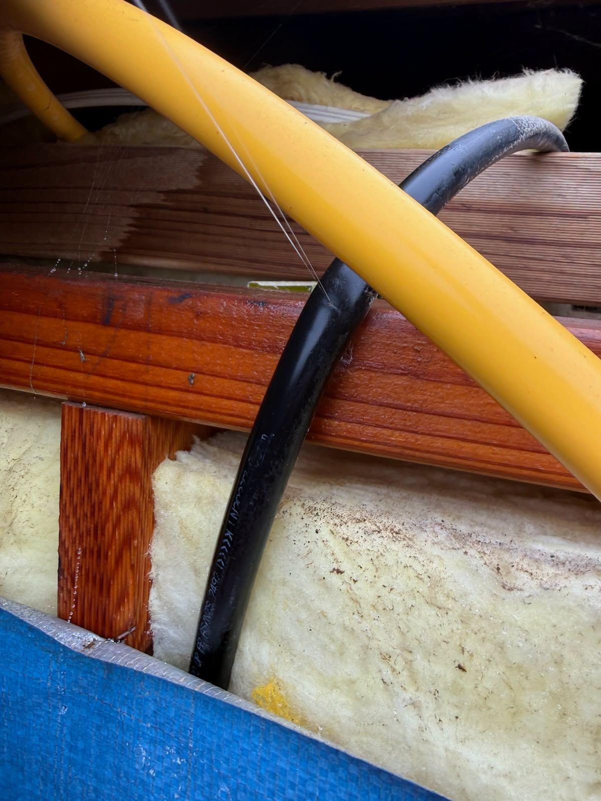 Close-up Of Yellow and Black Cables Crossing Wooden Beams and Insulation — Kerney Plumbing in Caroline Spring, VIC