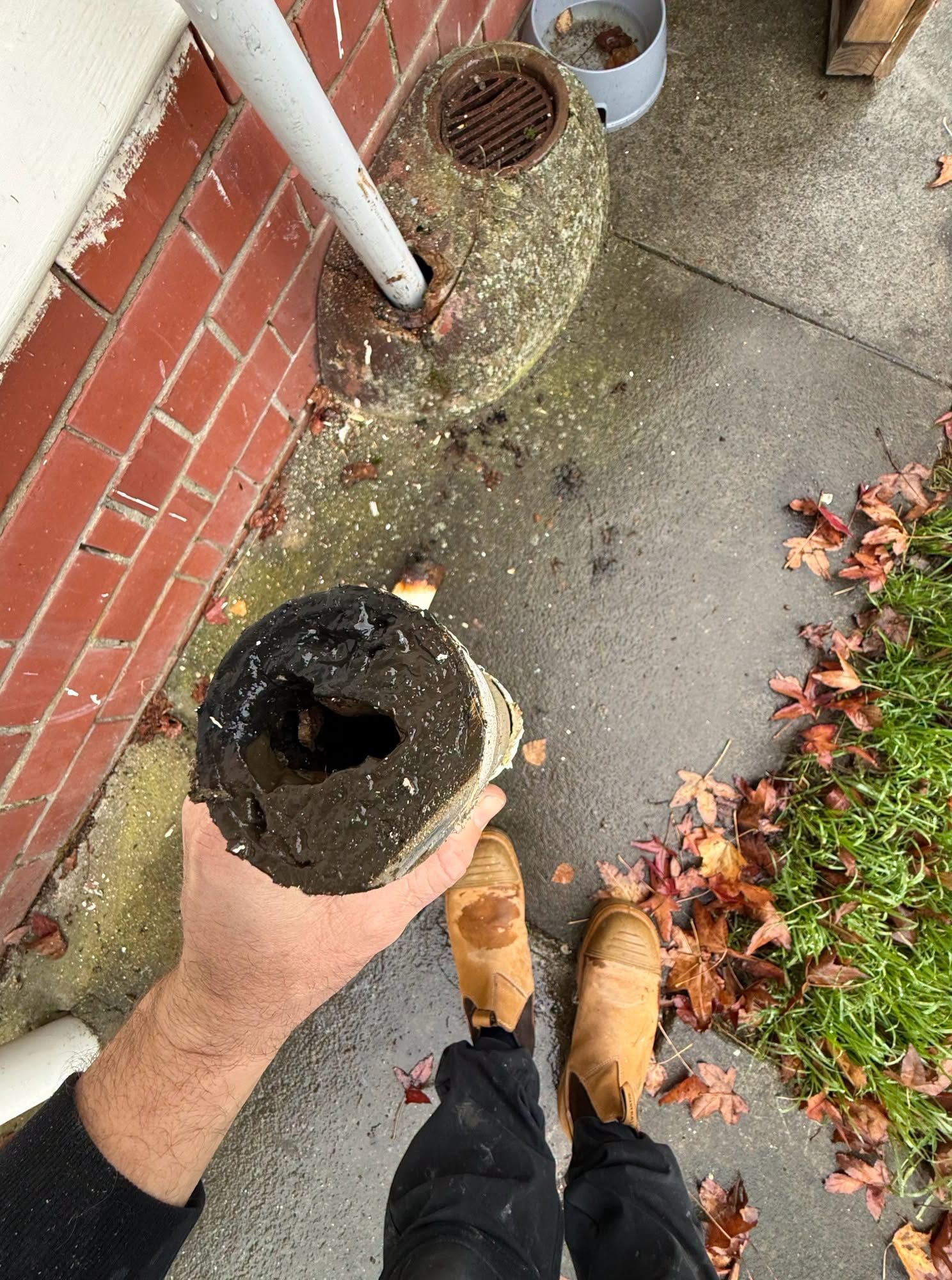 Person Holding a Broken Black Pipe Beside a Brick Wall and Sidewalk — Kerney Plumbing in Bacchus Marsh, VIC