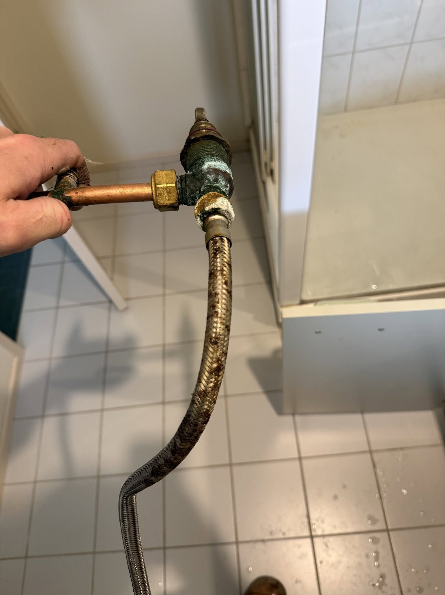 Hand Holding a Hose Connected to a Valve in a Tiled Bathroom — Kerney Plumbing in Bacchus Marsh, VIC
