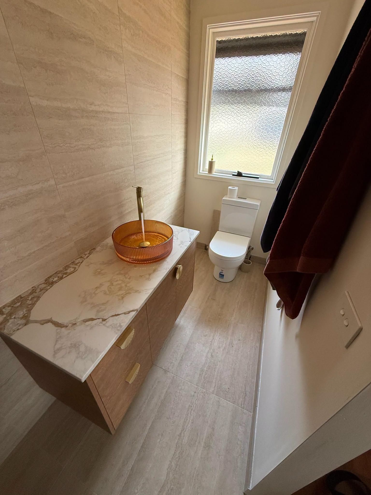 Narrow Bathroom With Marble Vanity, Orange Sink Bowl, Toilet, and Frosted Window With Burgundy Curtain— Kerney Plumbing in Ballarat, VIC