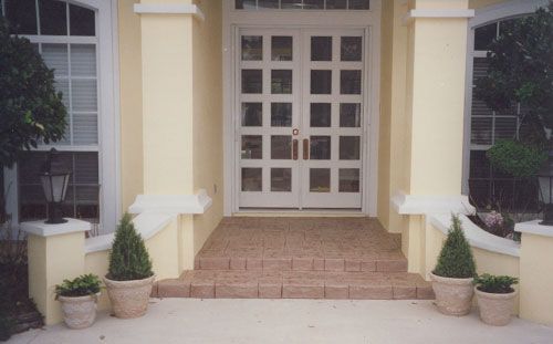 Yellow exterior with double glass doors, steps, planters, and columns.