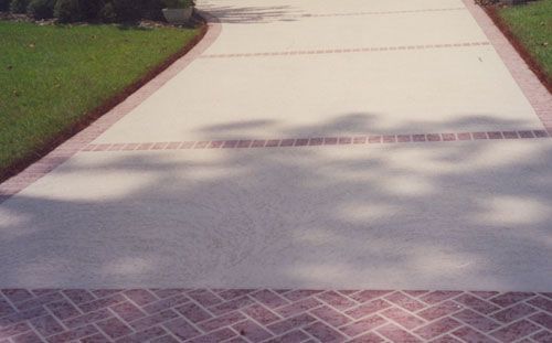 Concrete driveway with brick borders, lined with grass. Shadows of trees cast on the surface.
