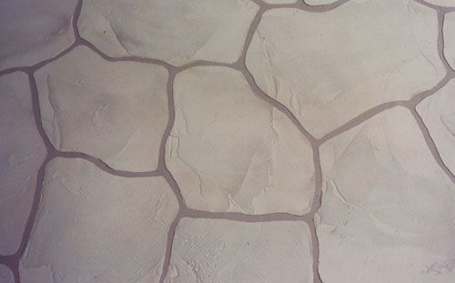 Close-up of a light-colored wall with a stone-like pattern, featuring gray grout lines and irregular stone shapes.