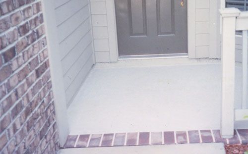Small front porch with concrete floor, brick border, and front door.