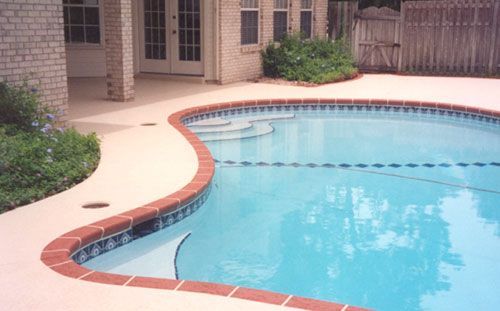 Swimming pool with red brick border, concrete patio, and adjacent building.