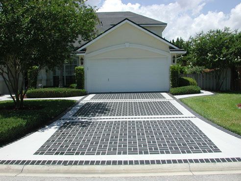 Driveway with decorative brick pattern leading to a two-car garage; green lawn and landscaping around the house.
