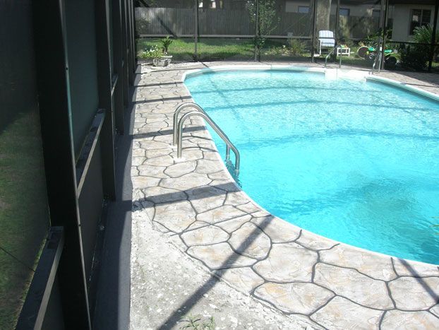 Pool with stone coping, a handrail, and screened enclosure on the left. Blue water.