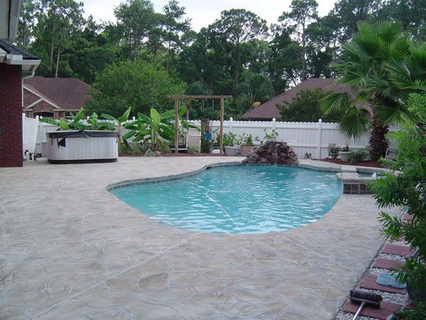 Backyard with pool, hot tub, and lush landscaping, enclosed by a white fence and trees.