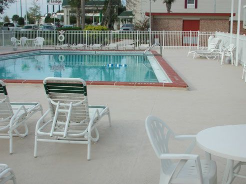A pool with white lounge chairs, a table, and a white fence, at an outdoor setting.