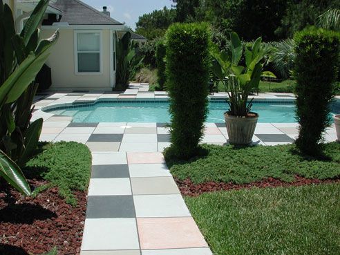 Pool with tiled pathway, flanked by greenery and topiaries. House in the background.