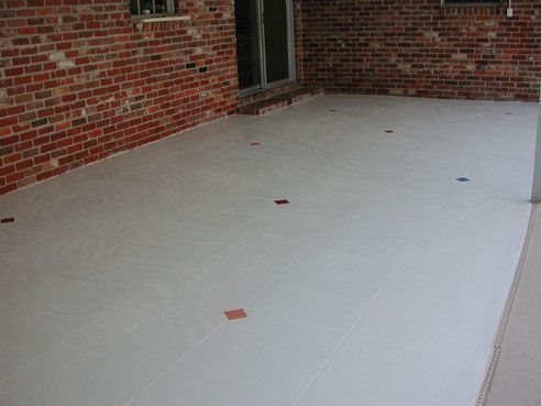 Concrete patio with a red brick wall and several colored tiles embedded.