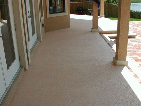 Tan concrete patio with support columns and brick border.