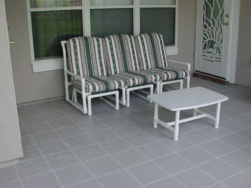 Outdoor seating area: white PVC sofa and table, striped cushions, gray tiled floor, neutral walls, and a white door.