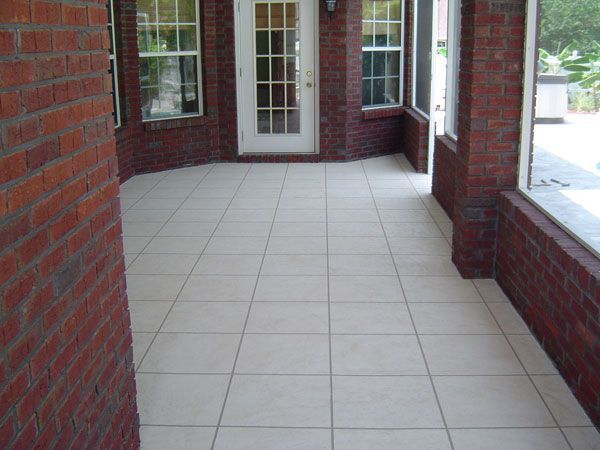 Red brick porch with light-colored tiled floor, leading to a white door and windows.