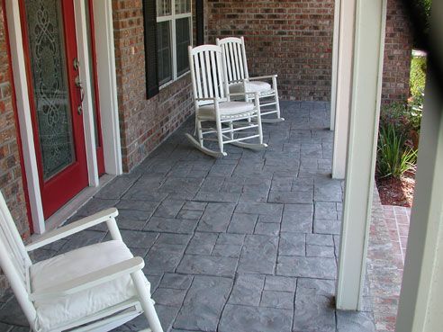 Three white rocking chairs on a gray stone patio, next to a red door on a brick porch.