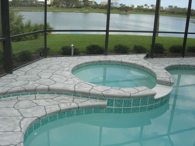 Pool with built-in hot tub, concrete deck, screened enclosure, overlooking a lake. Turquoise tile, blue water.