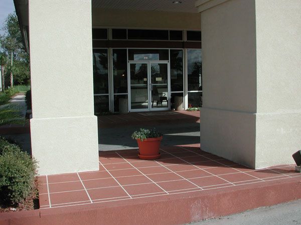 Hotel entrance with red-tiled floor, cream columns, and a potted plant. Glass doors lead inside.