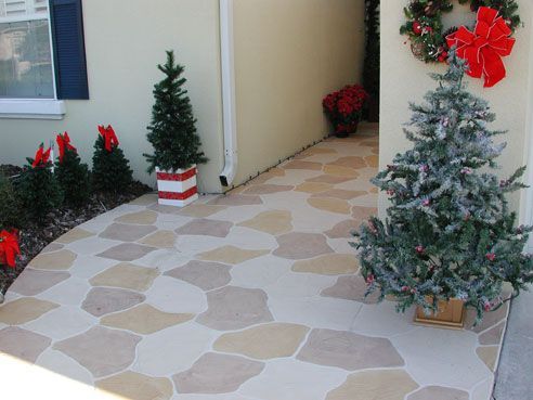 Holiday decorations on a walkway with a stone pattern. Trees, wreaths, and red bows add a festive touch.