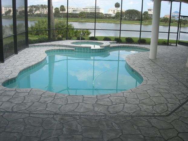 Indoor pool with blue water and gray stone edging, surrounded by a screen enclosure overlooking a body of water.
