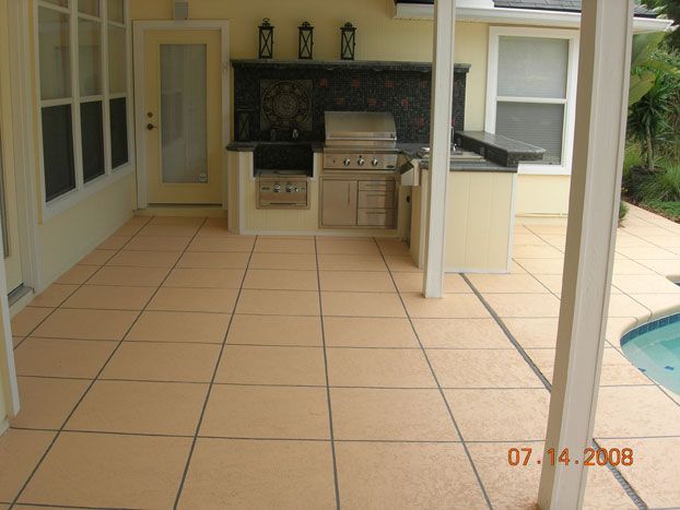 Outdoor kitchen with built-in grill and countertops on a tiled patio near a pool.