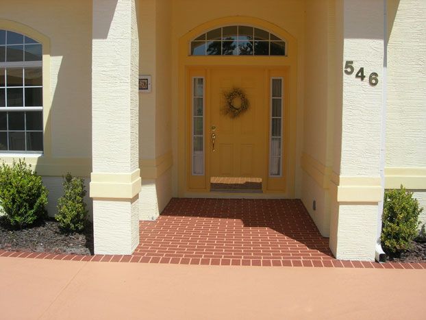 Yellow front door with sidelights, brick floor, and cream columns; house number 546.