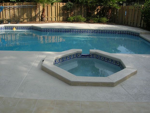 Swimming pool and connected spa with blue tile trim, surrounded by light-colored concrete patio.