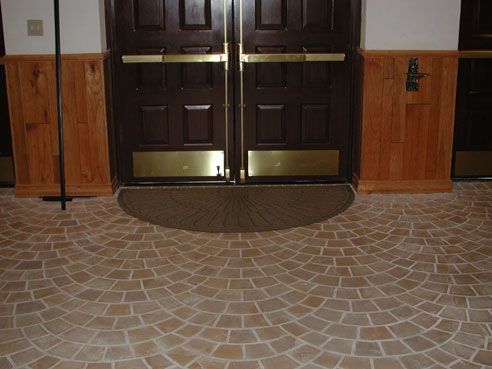 Brown doors with gold bars and a semi-circular doormat on a brick floor.