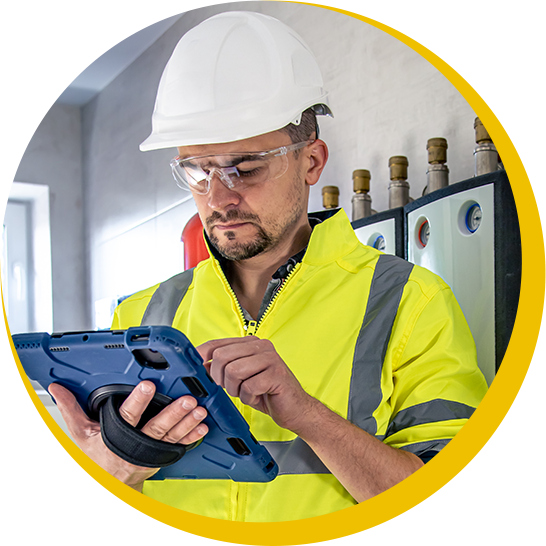 A man wearing a hard hat and safety vest is using a tablet
