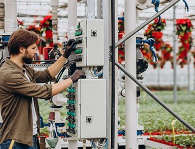 A man is working on a machine in a greenhouse.