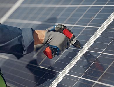 A man is working on a solar panel with a drill.